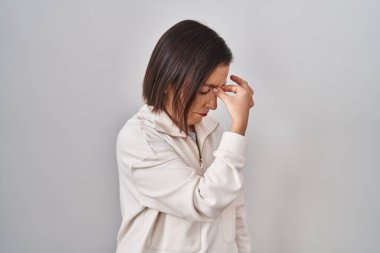 Orta yaşlı İspanyol bir kadın izole edilmiş arka planda duruyor. Burnu ve gözleri ovuşturmaktan yorulmuş, yorgunluk ve baş ağrısı çekiyor. Stres ve hüsran kavramı. 