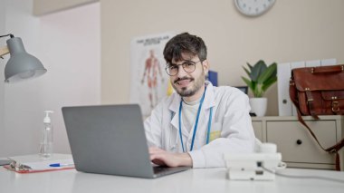Young hispanic man doctor using laptop working at clinic