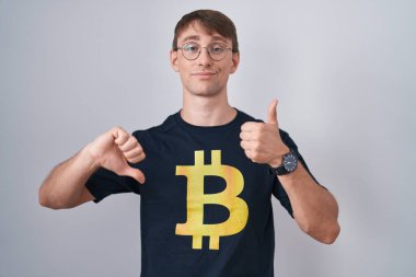 Bitcoin tişörtü giyen beyaz, sarışın bir adam. Baş parmak hareketi yapıyor. Anlaşmazlık ve anlaşma ifadesi. çılgın çatışma 