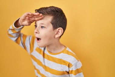 Sarı arka planda duran genç beyaz çocuk çok mutlu ve gülümsüyor. arama kavramı. 