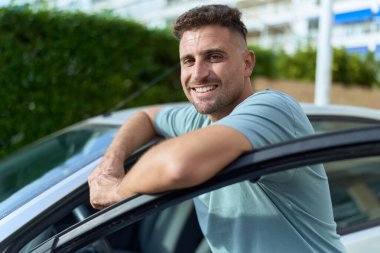 Genç İspanyol adam gülümsüyor. Sokakta araba kapısını açıyor.