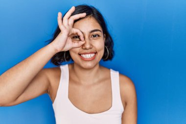 Mavi arka planda duran genç İspanyol kadın el hareketleriyle gülümsüyor ve mutlu yüzüyle parmaklarının arasından bakıyor.. 