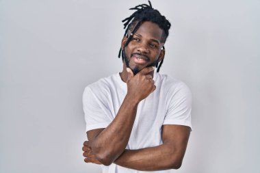 Beyaz arka plan üzerine günlük tişört giyen Afrikalı adam kameraya kollarını kavuşturmuş ve çenesini kaldırmış şekilde gülümsüyor. Olumlu düşünmek. 