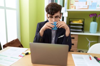 Non binary man business worker using laptop drinking coffee at office