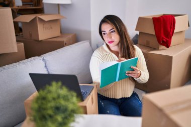 Genç ve güzel İspanyol kadın dizüstü bilgisayar kullanıyor. Yeni evinde deftere yazıyor.