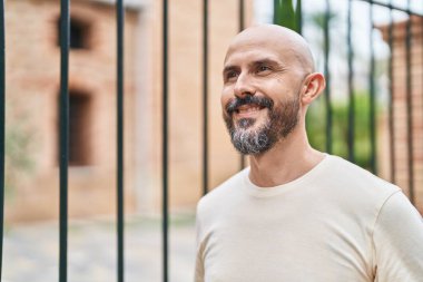 Genç kel adam gülümsüyor. Kendinden emin bir şekilde caddeye bakıyor.