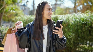 Parkta akıllı telefon kullanan genç ve güzel bir İspanyol kadın.