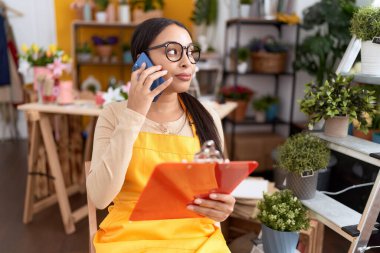 Çiçekçide akıllı telefondan konuşan genç Arap kadın çiçekçi.
