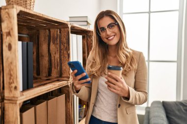 Akıllı telefon kullanan ve psikoloji merkezinde kahve içen genç sarışın kadın psikolog.