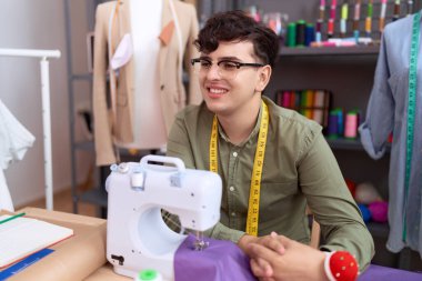 Non binary man tailor smiling confident sitting on table at atelier