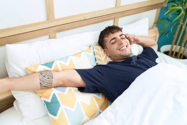 stock image Young hispanic man waking up stretching arms at bedroom