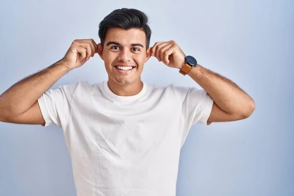Hispanic Man Standing Blue Background Smiling Pulling Ears Fingers Funny — Stock Photo, Image