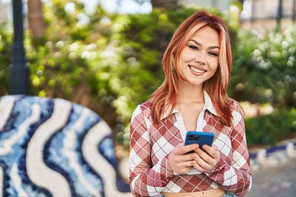 Genç Beyaz Kadın Parkta Akıllı Telefon Kullanarak Gülümsüyor — Stok fotoğraf