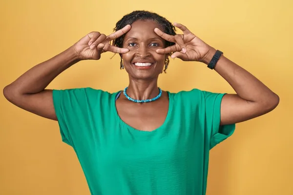 Африканская Женщина Дредами Желтом Фоне Делает Символ Мира Пальцами Лице — стоковое фото