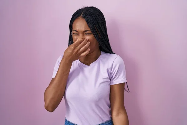 ピンクの背景の上に立っているアフリカ系アメリカ人の女性は 臭いと嫌な 耐え難い匂いを嗅ぎ 鼻の上に指で息を保持しています 臭いが悪い — ストック写真