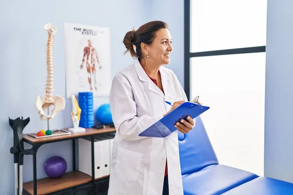Middle Age Hispanic Woman Physiotherapist Writing Clipboard Rehab Clinic — Stok fotoğraf
