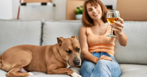 Young caucasian woman drinking wine sitting on sofa with dog at home