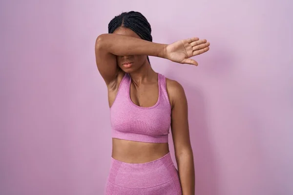 戴辫子的非洲裔美国女人身穿运动服 背景粉色 用胳膊蒙住眼睛 看起来严肃而忧郁 躲藏和拒绝的概念 — 图库照片