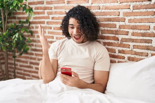 Hispanic Man Med Lockigt Hår Med Smartphone Sitter Sängen Firar — Stockfoto