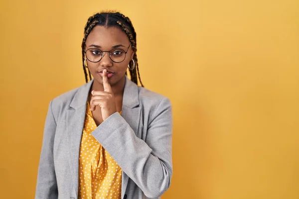 黄色い背景の上に立っているアフリカ系アメリカ人の女性は 唇に指で静かにするように求めています 沈黙と秘密の概念 — ストック写真