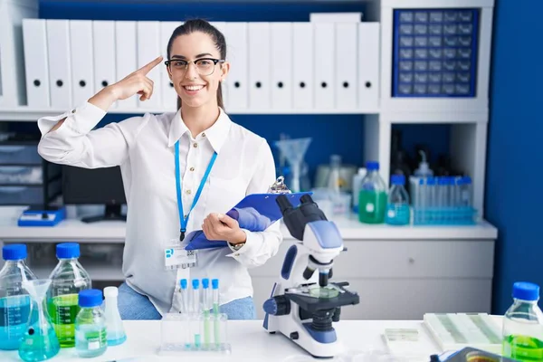Giovane Donna Bruna Che Lavora Laboratorio Scientifico Sorridendo Indicando Testa — Foto Stock