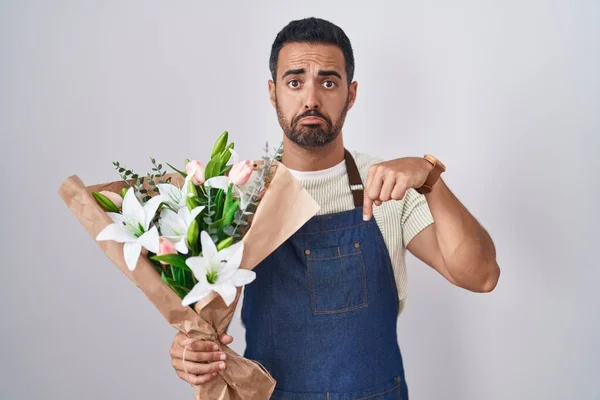 Hispanic man with beard working as florist pointing down looking sad and upset, indicating direction with fingers, unhappy and depressed.