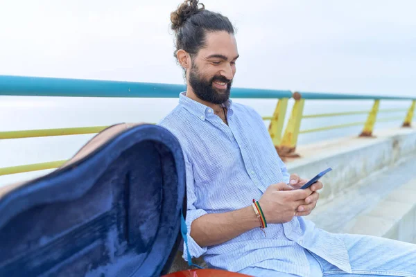 Ung Latinamerikansk Man Musiker Med Smartphone Sitter Bänk Vid Havet — Stockfoto