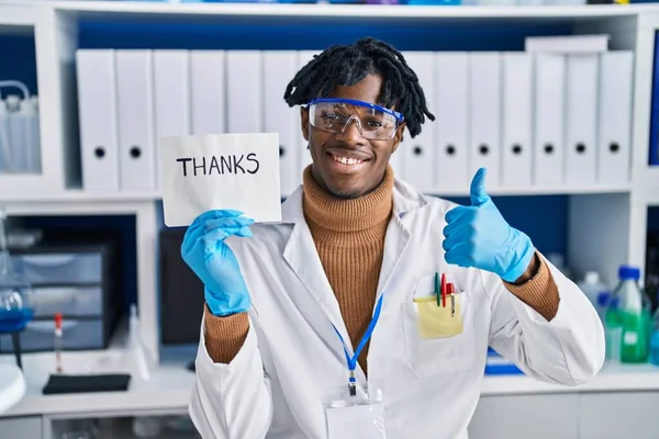 科学者研究所で働いている若いアフリカ人の男は笑顔で幸せと肯定的な 親指アップ素晴らしいと承認サインを行う — ストック写真