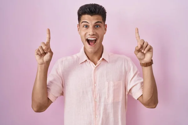 Young Hispanic Man Standing Pink Background Smiling Amazed Surprised Pointing — Stock Fotó