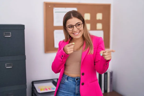 Young blonde woman standing at the office pointing fingers to camera with happy and funny face. good energy and vibes.