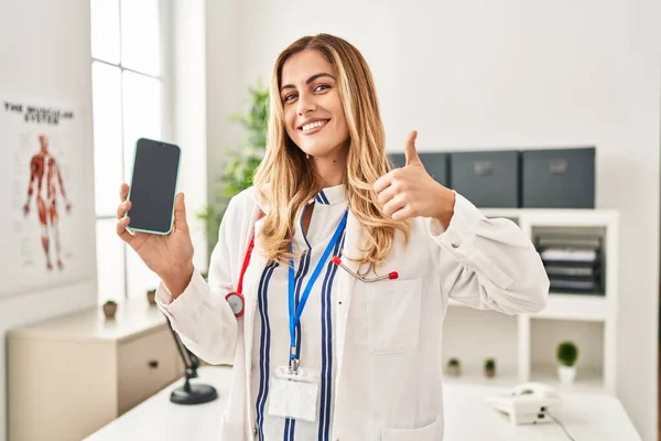 Young Blonde Doctor Woman Working Clinic Showing Smartphone Screen Smiling — Stock Photo, Image