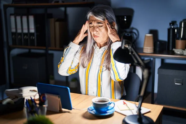 ストレスが原因で頭の痛みのために頭の上に手で夜のオフィスで働く白髪の中年女性 片頭痛 — ストック写真
