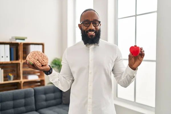 Hombre Afroamericano Que Trabaja Oficina Terapia Sosteniendo Cerebro Corazón Sonriendo —  Fotos de Stock
