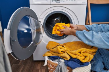 Young hispanic woman washing clothes at laundry room