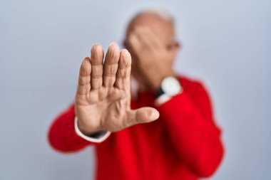 Senior man with grey hair standing over isolated background covering eyes with hands and doing stop gesture with sad and fear expression. embarrassed and negative concept. 