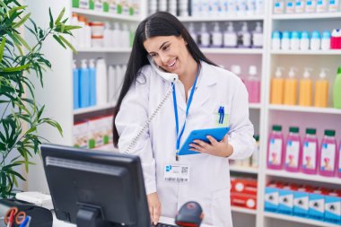 Genç ve güzel İspanyol kadın eczacı telefonda konuşuyor eczanede dokunmatik ped kullanıyor.