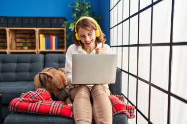 Genç ve güzel bir kadın kanepede oturmuş gülümsüyor mutlu ve pozitif, başparmağıyla mükemmel ve onay işareti yapıyor. 