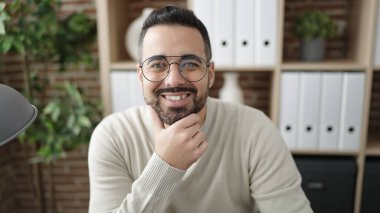 Young hispanic man business worker smiling confident sitting on table at office
