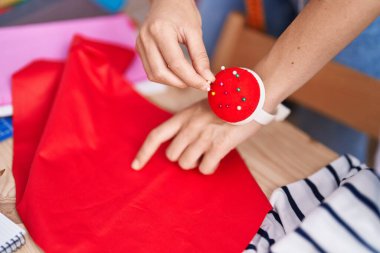 Young beautiful hispanic woman tailor holding pin at clothing factory