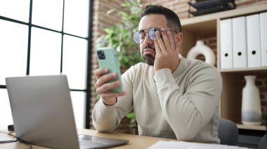 Genç İspanyol iş adamı ofiste akıllı telefon kullanıyor.