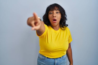 Mavi arka planda dikilen İspanyol kadın parmağı önde, ağzı açık, şaşırmış bir ifade, ön tarafta bir şey var. 