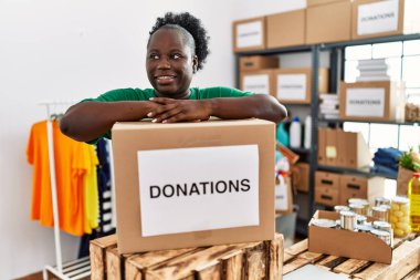 Gönüllü üniforma giyen Afro-Amerikalı genç bir kadın hayır kurumunda bağış paketine yaslanıyor.