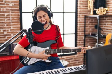 Genç kadın sanatçı müzik stüdyosunda elektro gitar çalarak şarkı söylüyor.