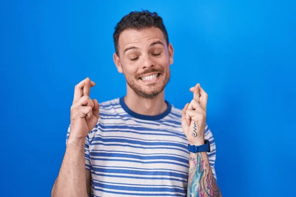 Young Hispanic Man Standing Blue Background Gesturing Finger Crossed Smiling — Stock Photo, Image