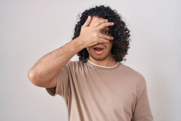 Hispánec Kudrnatými Vlasy Stojící Nad Bílým Pozadím Vykukující Šoku Zakrývající — Stock fotografie