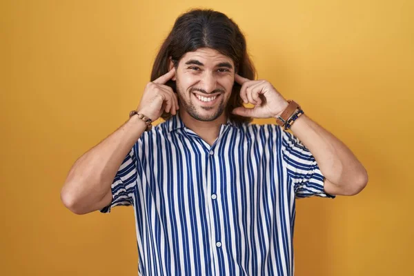 Hispanic Man Long Hair Standing Yellow Background Covering Ears Fingers — Stock Photo, Image