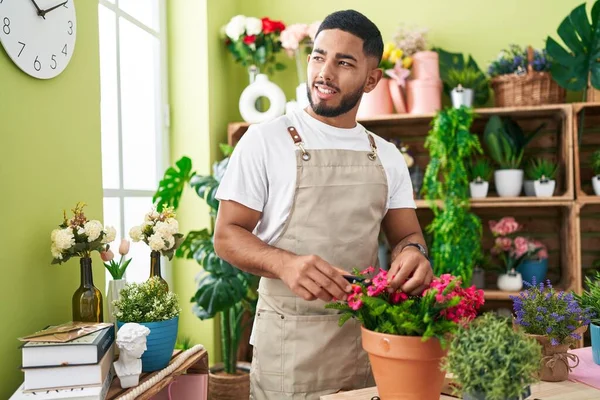 Young latin man florist cutting plants at flower shop