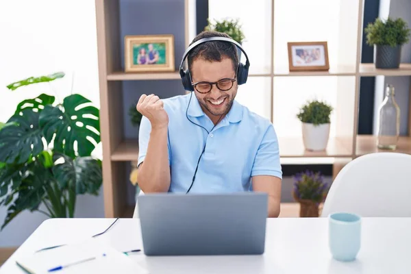 ヘッドフォンを身に着けているコンピュータのラップトップを使用して働いているヒスパニック系の男は誇りに思って叫んで 勝利と成功を祝う非常に腕を上げ — ストック写真