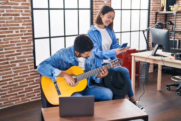 男性と女性のミュージシャンが音楽スタジオでスマートフォンを使ってクラシックギターを演奏 — ストック写真