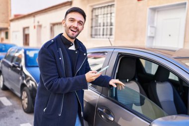 Young hispanic man using smartphone leaning on car at street